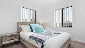 Ein Schlafzimmer mit einem Bettgestell aus Holz, weißer Bettwäsche und Blick durch Jalousien.