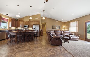 A spacious kitchen with a central island, bar stools, and a large brown leather sofa in a living area with a view.
