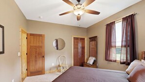 Une chambre à coucher avec un lit, un ventilateur de plafond, des portes en bois, un miroir et une fenêtre avec des rideaux.