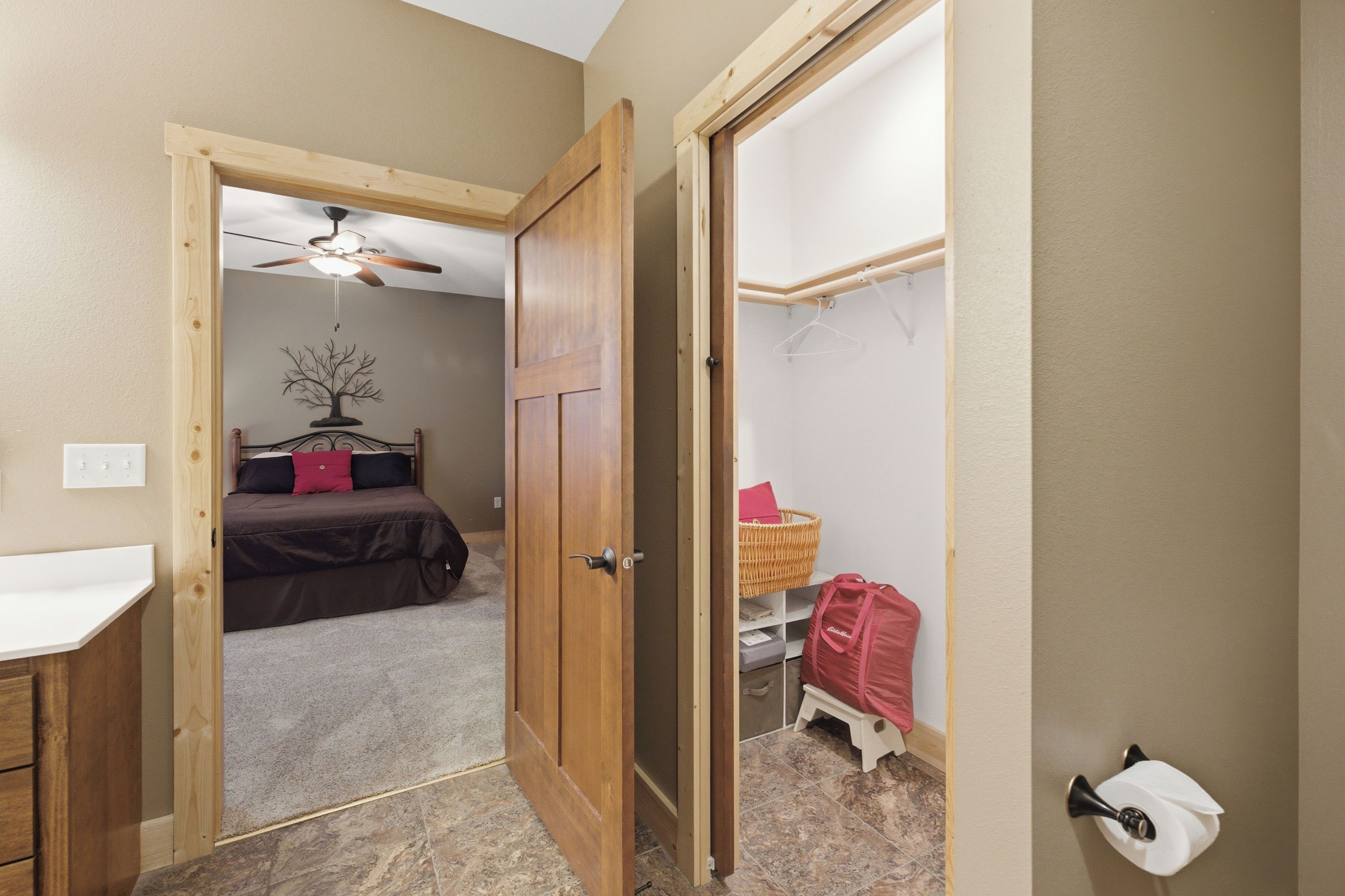 A bedroom with a bed, a ceiling fan, a wall-mounted tree decoration, and a door leading to another room.