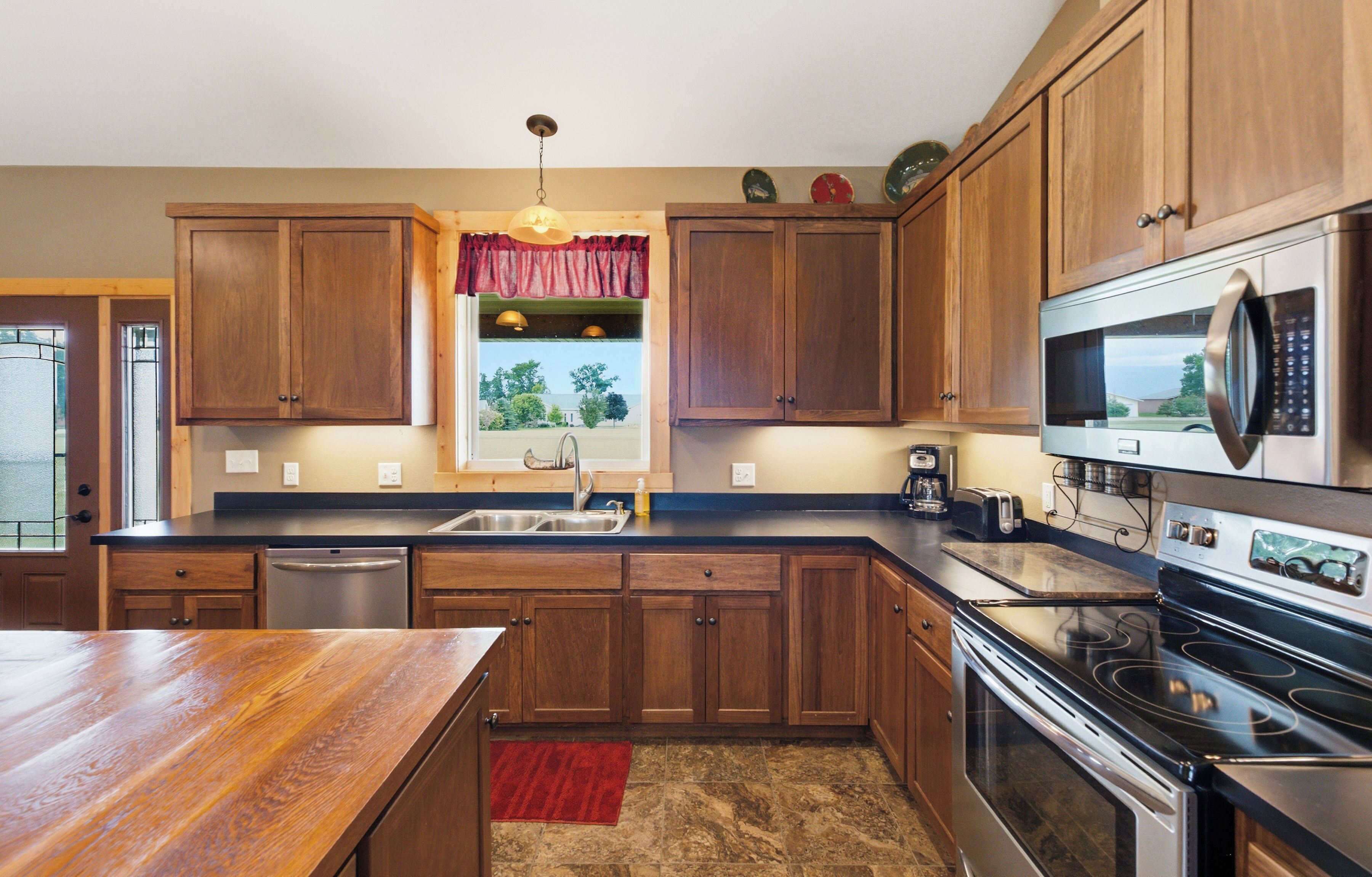 Una cuina amb armaris de fusta, electrodomèstics d'acer inoxidable, un doble mànec i una finestra amb vista a l'exterior.