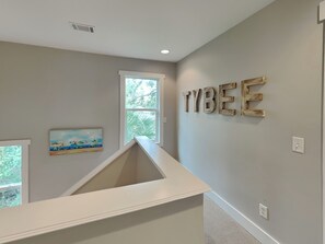 Ein Zimmer mit schrägem Dach, einem Fenster mit Blick auf Bäume und einer Wand mit der Aufschrift "TYBEE" im rustikalen Stil.