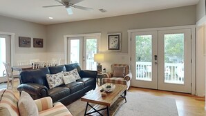 A spacious living room with a leather sofa, striped armchairs, a wooden coffee table, and a ceiling fan. - Billfish | Upgraded, All En Suites, Great Location (Tybee Island)