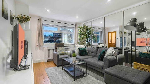 Ein modernes Wohnzimmer mit einem grauen Sofa, einem Couchtisch und einem Fernseher. Ein Fenster bietet Blick auf Gebäude.