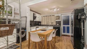Eine kleine Küche mit einem Holztisch, weißen Stühlen und einem schwarzen Kühlschrank.