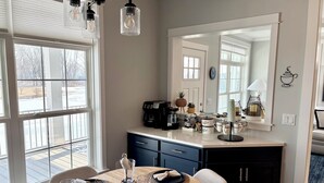 A dining area with a wooden table set for four, a coffee station, and a large mirror above the counter. - Perfect 3-bedroom house with AC in soothing Waterview @ Baypoint (Lakeside Marblehead)