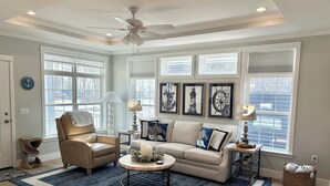 A living room with a beige sofa, a round coffee table, a beige armchair, and a ceiling fan. There are three framed nautical-themed pictures on the wall. - Perfect 3-bedroom house with AC in soothing Waterview @ Baypoint (Lakeside Marblehead)