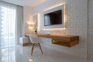 Ein modernes Hotelzimmer mit weißer Ziegelwand, einem Wand-Fernseher, einem hölzernen Schminktisch, einem weißen Sessel und einem kleinen weißen Hocker.