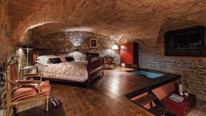 A bedroom with a stone wall, a wooden bed, a red cabinet, a chair, a small table, and a pool. - Loft with Stone vaults in Villa Storica (Matraia)