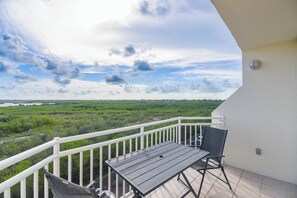 A balcony with a table and chairs, overlooking a green landscape and a body of water. - The Grand Turk | Spectacular Sunset View, Private (Key West)