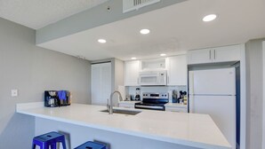 A modern kitchen with a central island, white cabinetry, stainless steel appliances, and blue bar stools. - The Grand Turk | Spectacular Sunset View, Private (Key West)