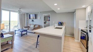 A modern kitchen with a central island, a dining area with a sofa and table, and a living room with a TV and artwork. - The Grand Turk | Spectacular Sunset View, Private (Key West)