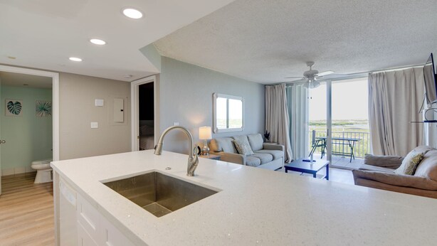 A modern kitchen with a large island, a dining area with a table and chairs, and a living room with a sofa and a view of the outdoors. - The Grand Turk | Spectacular Sunset View, Private (Key West)