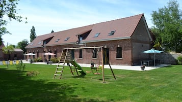 Ein Backsteinhaus mit geneigtem Dach, einer Schaukel und einer Terrasse mit Außenmöbeln.