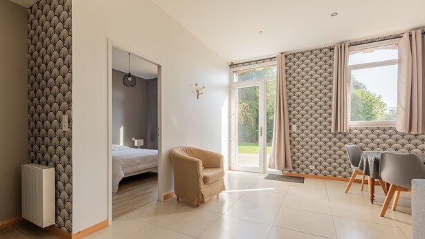 A modern living room with a sofa, a dining table with chairs, a radiator, and a patterned wallpaper. - Holiday Home 'Gite Clémentine' with Private Terrace, Shared Garden and Wi-Fi (Baromesnil)