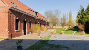 A brick building with multiple windows and doors, a gravel path, and a small garden area with potted plants. - Holiday Home 'Gite Baie De Somme' with Private Terrace, Private Garden and Wi-Fi (Baromesnil)