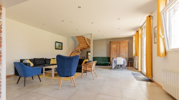 A spacious living area with a sofa, chairs, a dining table, a staircase, and a view of the outside. - Holiday Home 'Gite Baie De Somme' with Private Terrace, Private Garden and Wi-Fi (Baromesnil)