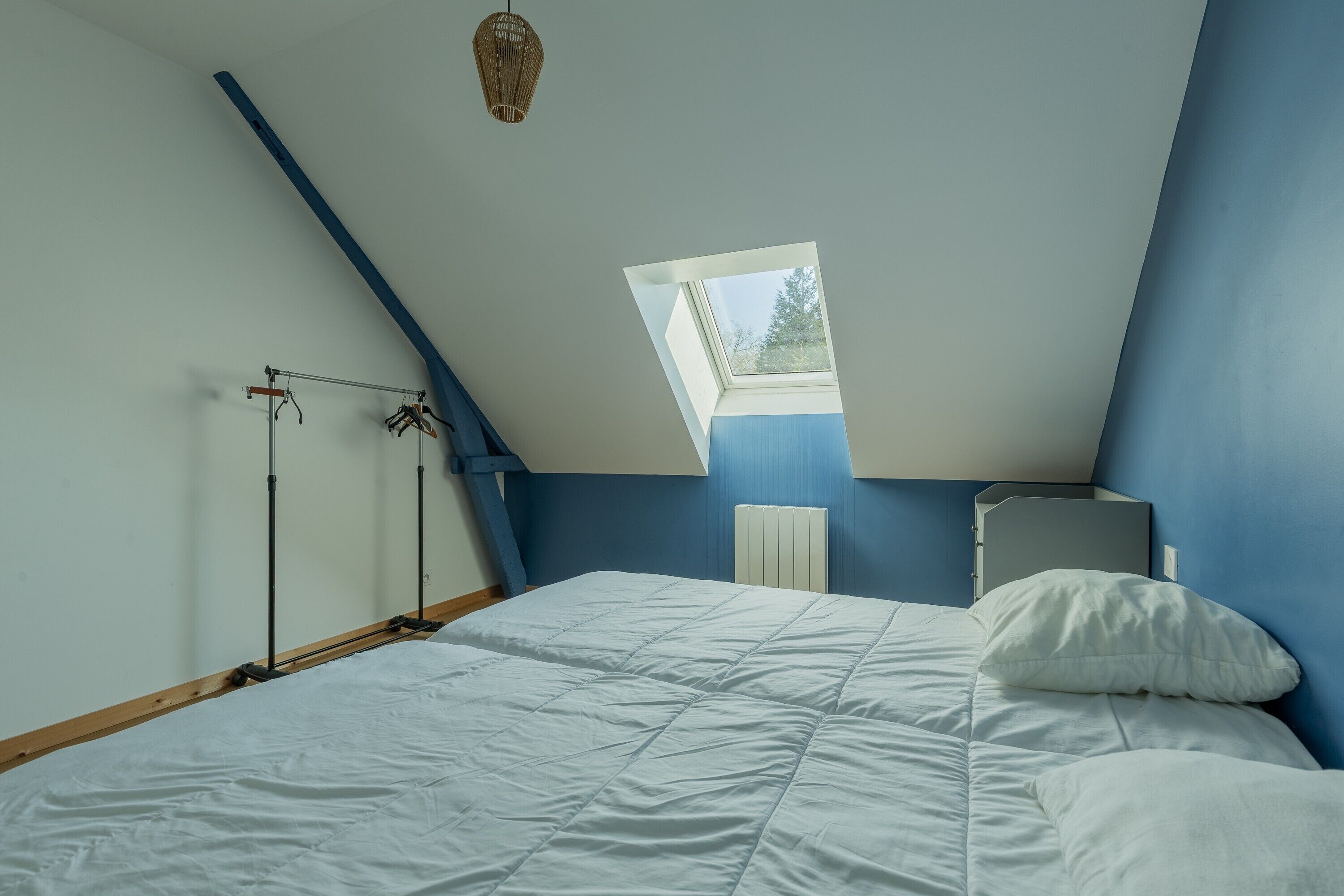 A bedroom with a sloped ceiling, a skylight, a bed with white bedding, and a radiator.