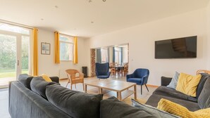 A modern living room with a sofa, armchairs, a coffee table, and a TV mounted on the wall. - Holiday Home 'Gite Baie De Somme' with Private Terrace, Private Garden and Wi-Fi (Baromesnil)