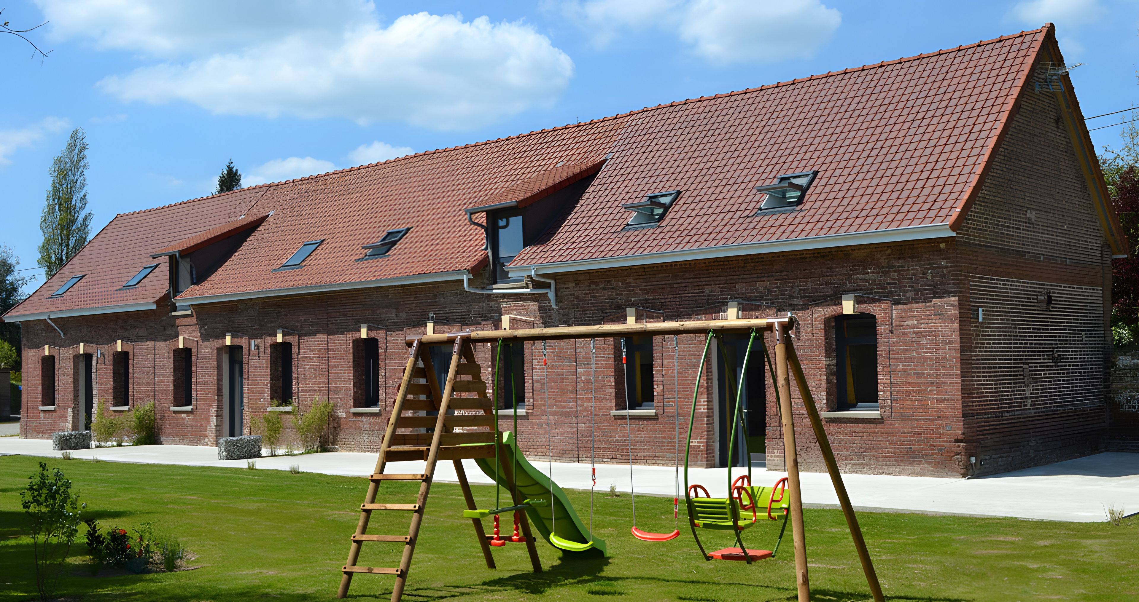 Un bâtiment en briques avec un toit en pente, une balançoire et un toboggan vert.