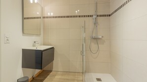 Ein modernes Badezimmer mit einer Duschkabine aus Glas, einem Waschbecken mit dunklem Unterschrank und einem Spiegel mit Beleuchtung darüber.