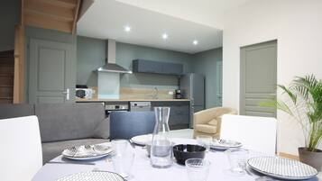 A modern dining area with a table set for four, a sofa, and a kitchen in the background.