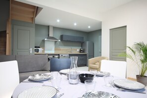 Un comedor moderno con una mesa dispuesta para cuatro personas, un sofá y una cocina al fondo.