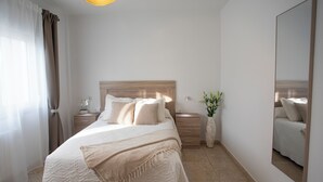 A bedroom with a large bed, a nightstand, a dresser, a mirror, and a vase with flowers.