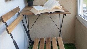 A corner with a wooden bench, a small table with an open book, a potted plant, and a bottle.