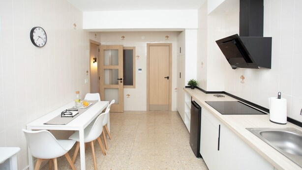 A modern kitchen with a dining area, featuring a white tiled backsplash, a black range hood, and a built-in dishwasher.