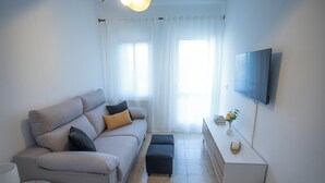 A modern living room with a sofa, ottoman, and a flat-screen TV mounted on the wall.