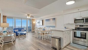 Una cocina moderna con armarios blancos, electrodomésticos de acero inoxidable y un comedor con mesa y sillas blancas.