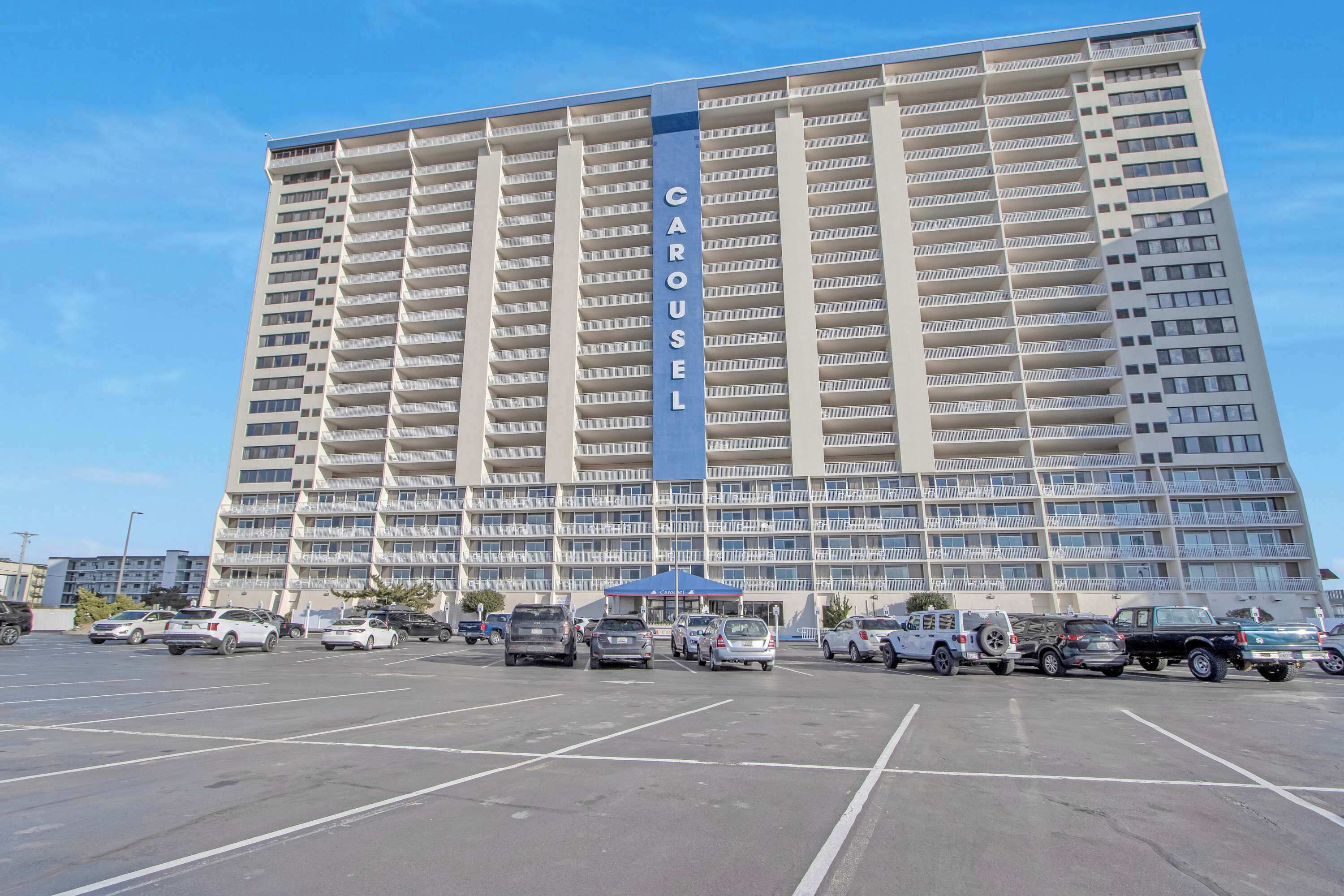 A high-rise hotel with a prominent "CAROUSEL" sign, featuring multiple balconies and a parking lot with various vehicles.