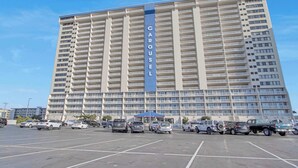 Un hotel de gran altura con un llamativo letrero que dice "CAROUSEL", con varios balcones y un estacionamiento con diferentes vehículos.