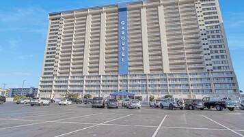A high-rise hotel with a prominent "CAROUSEL" sign, featuring multiple balconies and a parking lot with various vehicles.
