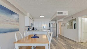 Una cocina moderna con armarios blancos, una mesa de comedor de madera y un cuadro grande en la pared.