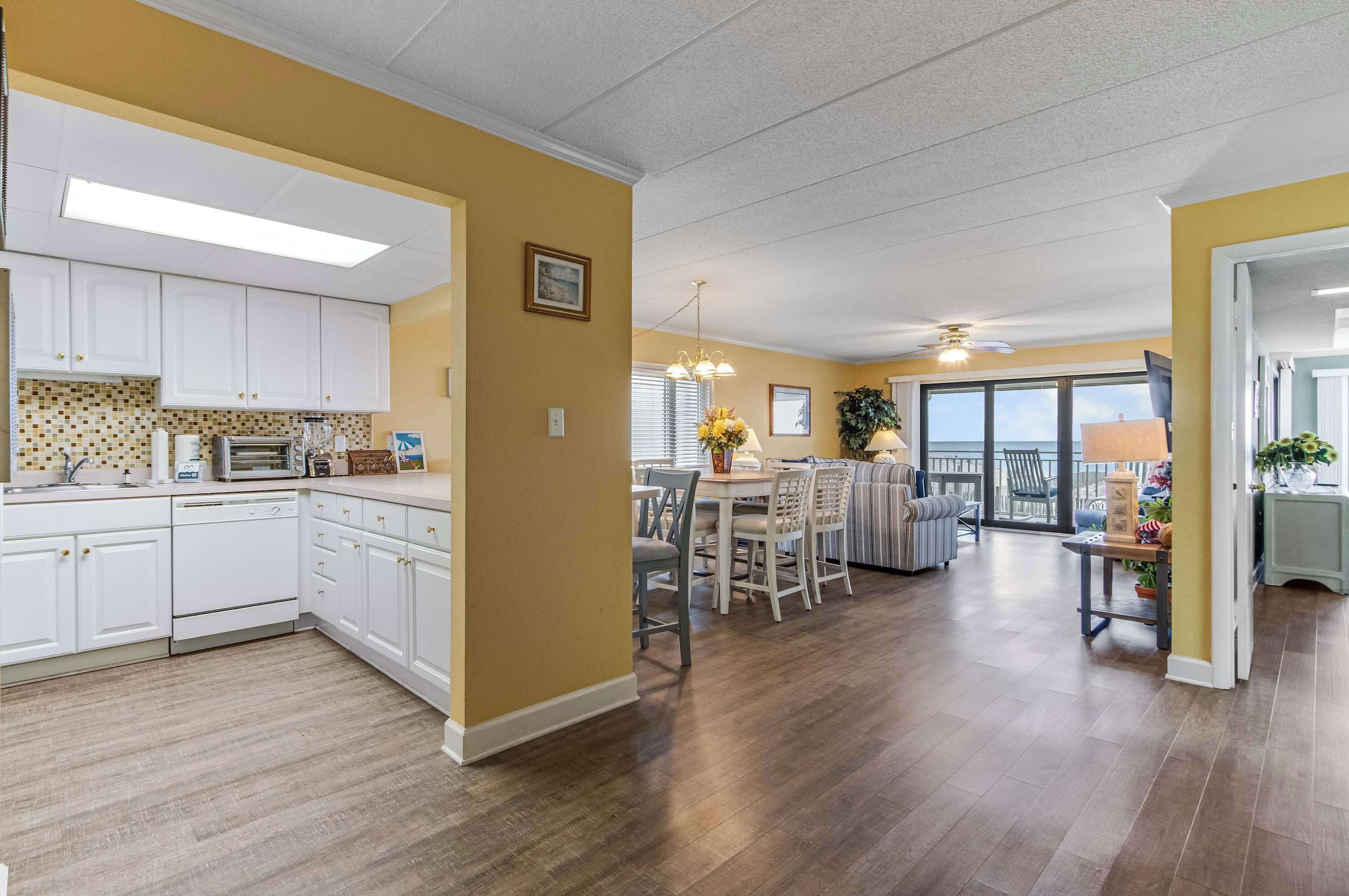A spacious kitchen with white cabinets, a dining area with a table and chairs, and a view of the outdoors through large windows.