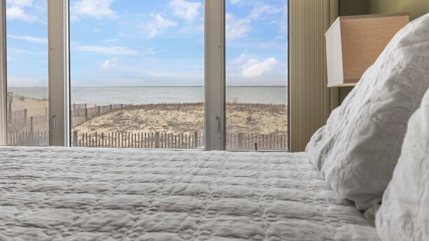 Un dormitorio con un ventanal grande con vistas a una playa y una valla de madera.