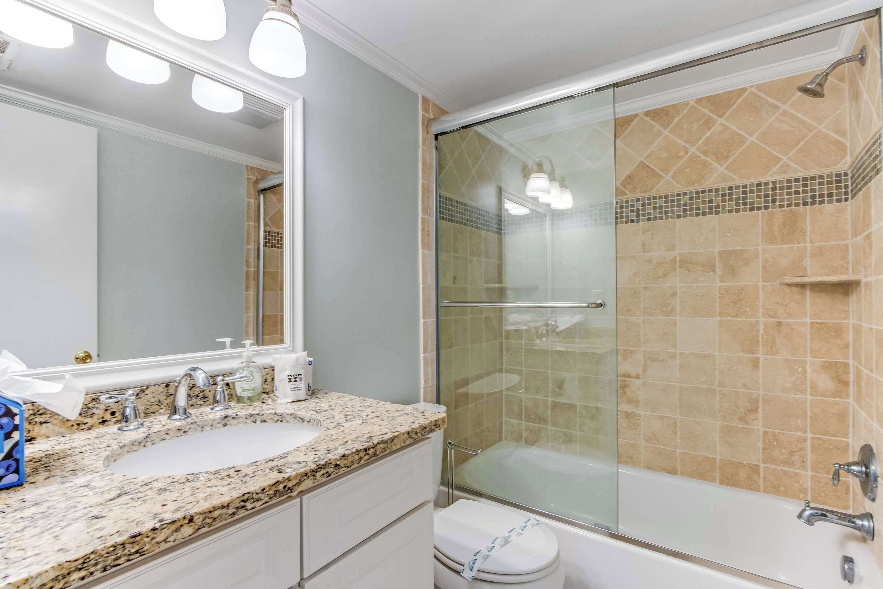 A bathroom with a granite countertop sink, a glass-enclosed shower, and a white toilet.