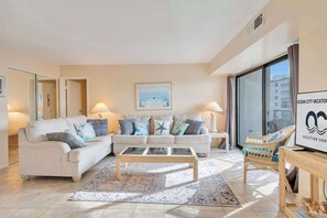 A spacious living room with a beige sofa set, a glass coffee table, and a wicker chair. - 9400 Building #407 (Ocean City)