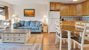Un salon confortable avec un canapé, une table basse et un coin repas comprenant une table et des chaises. Il y a aussi une cuisine avec des meubles en bois et un réfrigérateur.