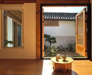 Ein traditioneller japanischer Raum mit Tatami-Böden, einer Schiebetür und Blick auf einen Garten mit einem kleinen Tisch und Tee-Service.