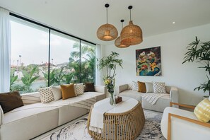 Ein modernes Wohnzimmer mit großem Fenster, einem runden Couchtisch und zwei Sofas mit gemusterten Kissen.