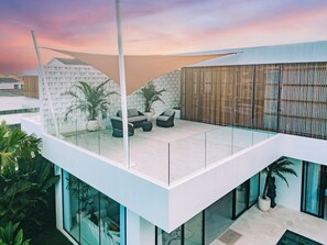 Ein modernes Gebäude mit Glasbalkon, Außenbereich mit Sitzgelegenheiten und Kübelpflanzen.