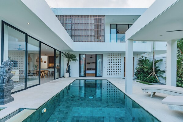 Ein modernes Haus mit einem zentralen Pool, Glaswänden und einem Essbereich.