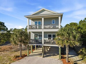 A two-story beachfront house with a balcony on the upper floor, surrounded by palm trees and a sandy beach. - Lightly Salted (Gulf Shores)