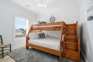 A bunk bed with a wooden frame and white bedding, a small chair, a window with blinds, and a wall-mounted ship's wheel decoration. - Lightly Salted (Gulf Shores)