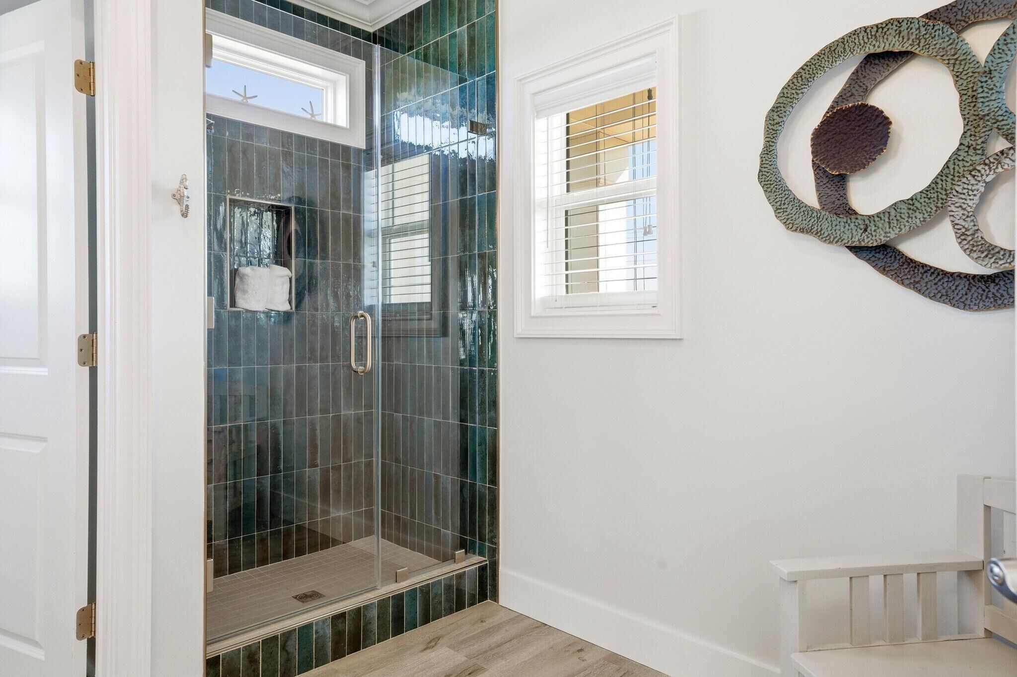 A bathroom with a glass shower enclosure, a towel rack, and a decorative wall piece.