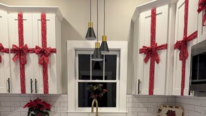 Eine moderne Küche mit weißen Schränken, einem Edelstahl-Geschirrspüler, einem schwarzen Herd und einem Fenster mit einem Adventskranz.