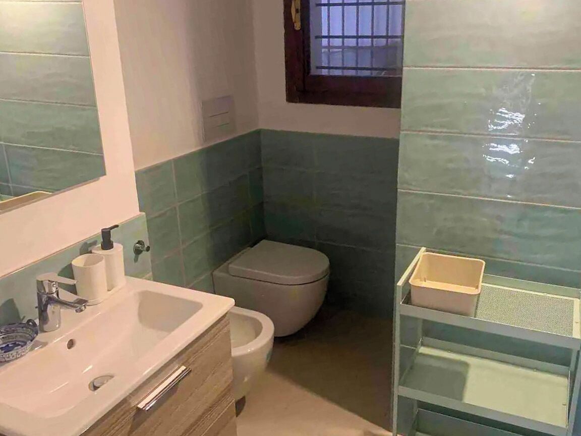 A bathroom with a sink, toilet, and a small window.